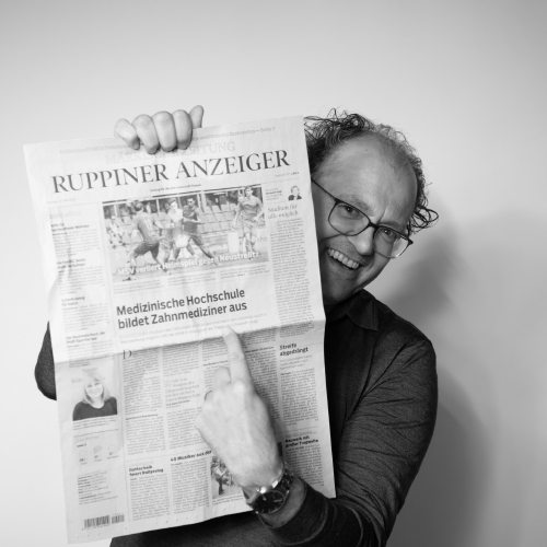 Mittelalter, weißer Mann mit Brille hält Titelseite einer Zeitung hoch und zeigt auf Artikel über die Einführung des neuen Zahnmedizin Studiums an der MHB